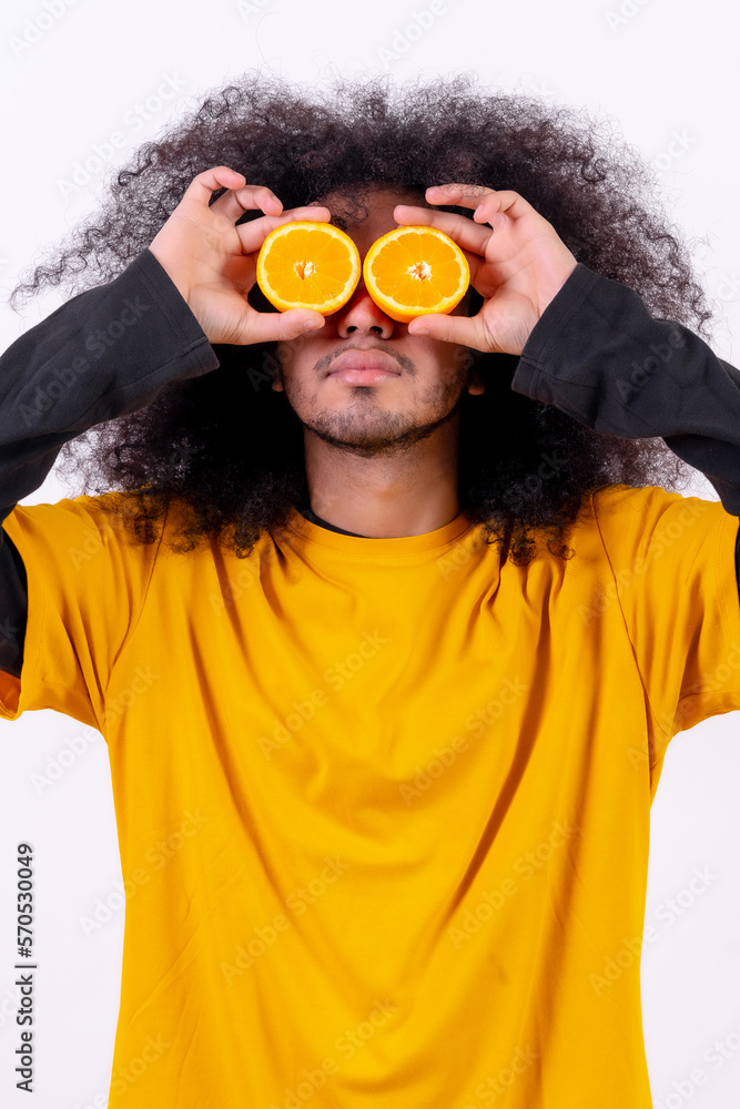 Portrait with the orange fruit in the eyes split in half. Young boy with afro hair on white background Portrait with the orange fruit in the eyes split in half. Young boy with afro hair on white background