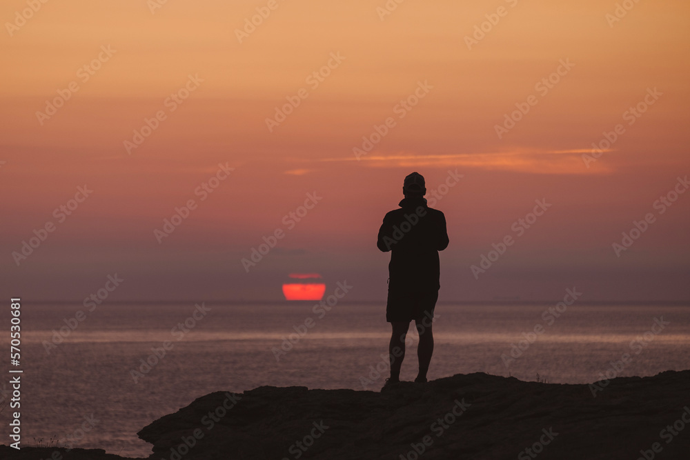 Young and watches sun rising in the distance as capture the moment on his phone. Young and watches sun rising in the distance as capture the moment on his phone.