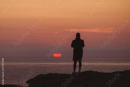 Young and watches sun rising in the distance as capture the moment on his phone. photo