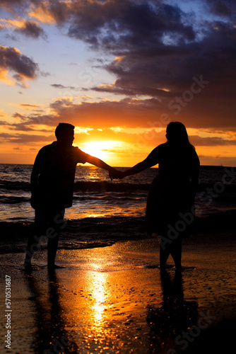A young couple walking on the beach at sunset photo