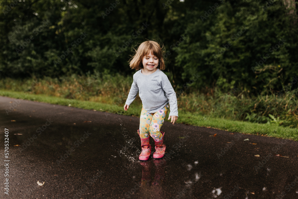 Young girl splashes in puddle on walking trail on a cloudy fall day Young girl splashes in puddle on walking trail on a cloudy fall day