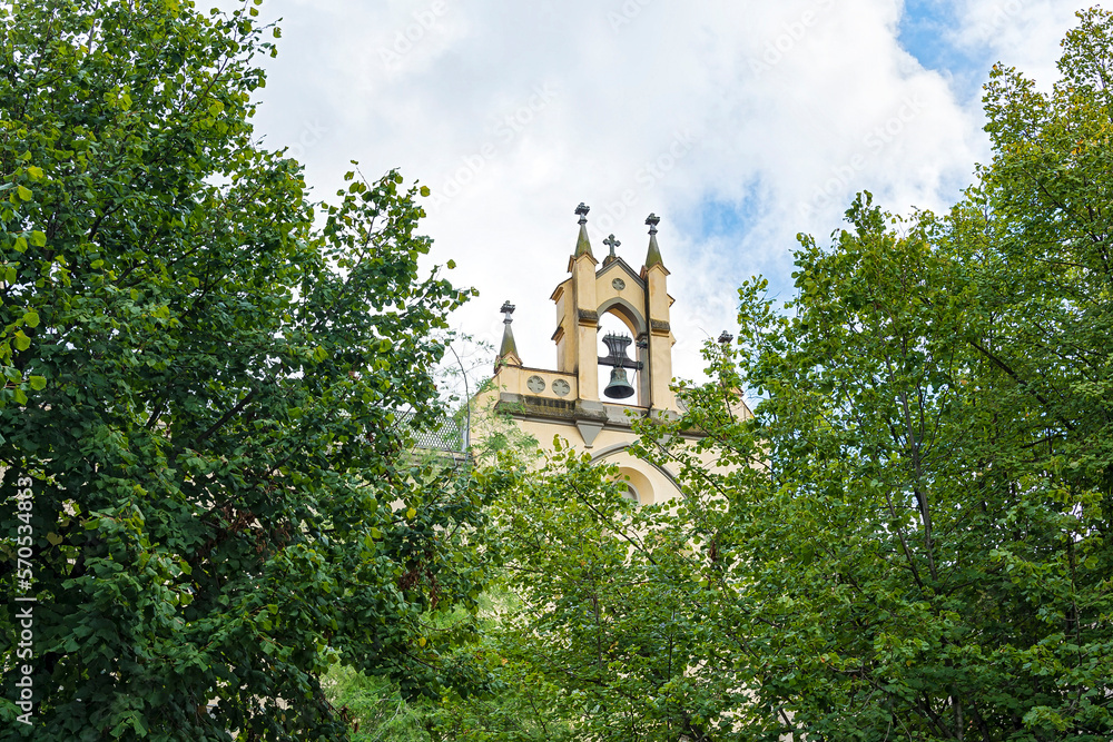 The old bell is seen behind the green tree branches (Girona, Spain)