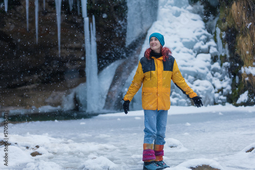 redhead young woman with red in a waterfall of nine in the mountain while snowing, copy space