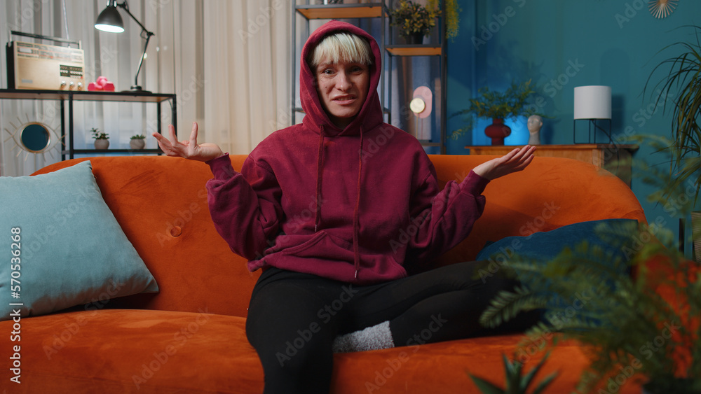 Obraz premium What. Why. Woman with short hair raising hands in indignant expression asking reason of failure demonstrating disbelief irritation by troubles at home apartment. Girl in evening room sitting on sofa