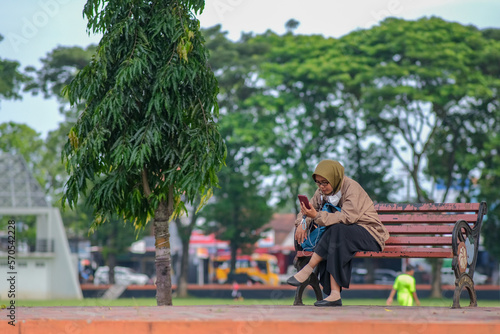 Woman sitting alone on a park bench in Kutoarjo, 5 February 2023