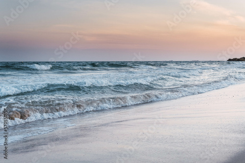 landscape of sea waves breaking on the beach shore against pink sunset