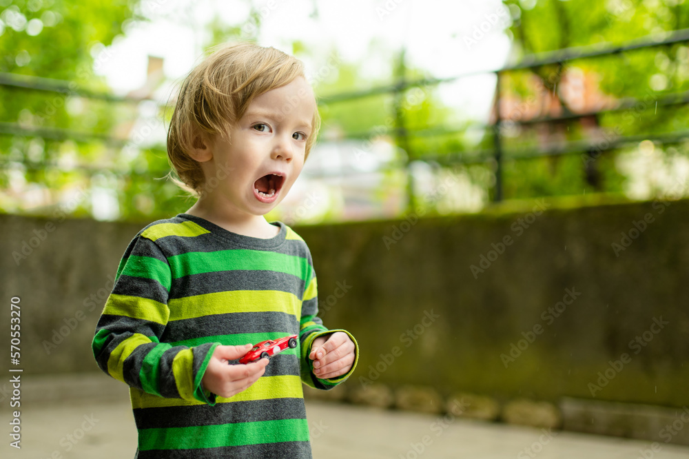Cute toddler boy playing with colorful toy cars outdoors. Cute toddler boy playing with colorful toy cars outdoors.