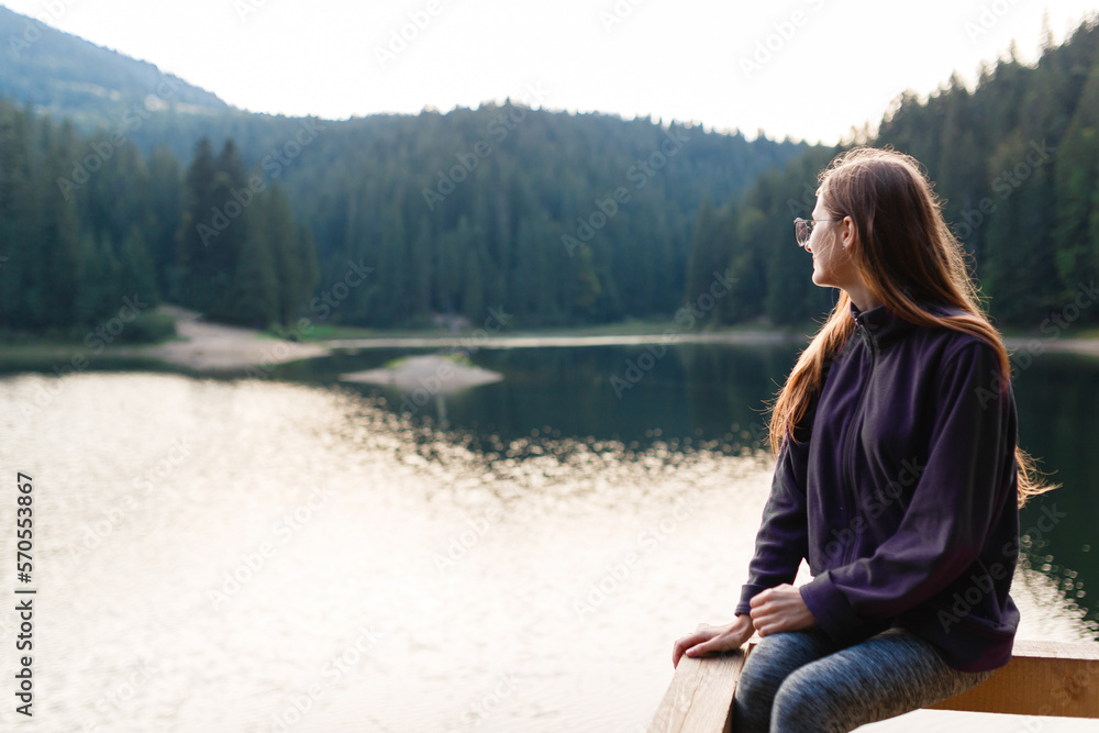 female tourist in a sweater and jeans near a mountain forest lake