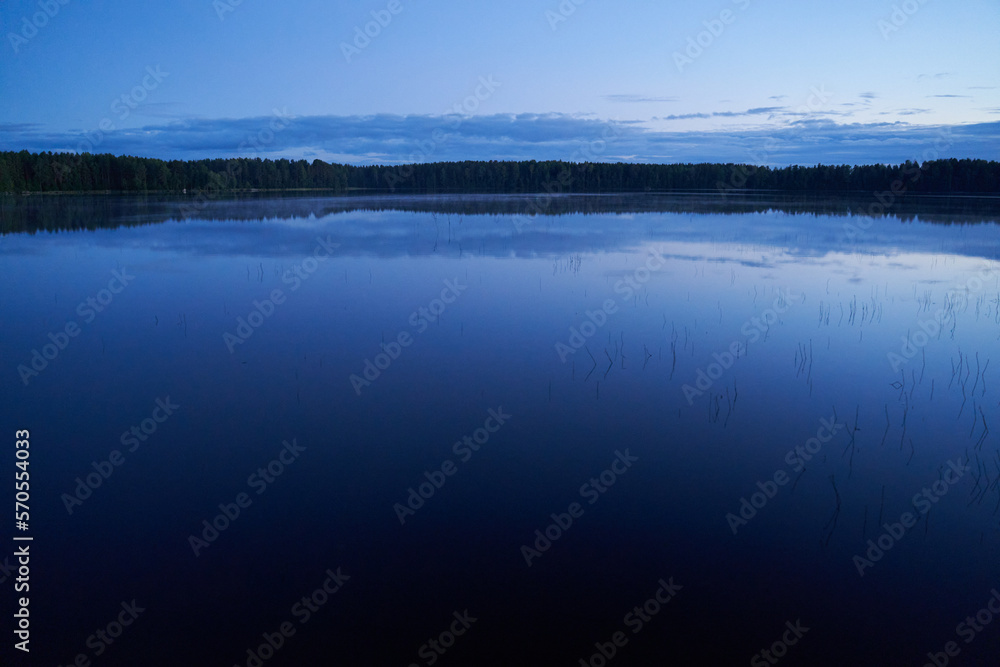 Evening landscape with a lake and forest mirroring in water.