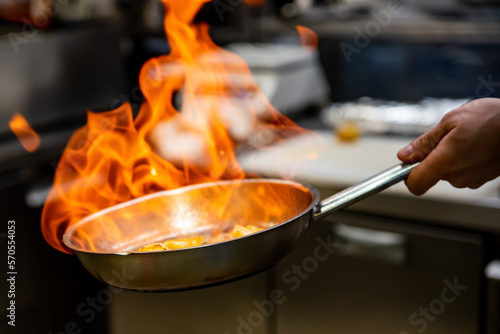 Chef hand in restaurant kitchen with pan, cooking flambe on shrimps photo