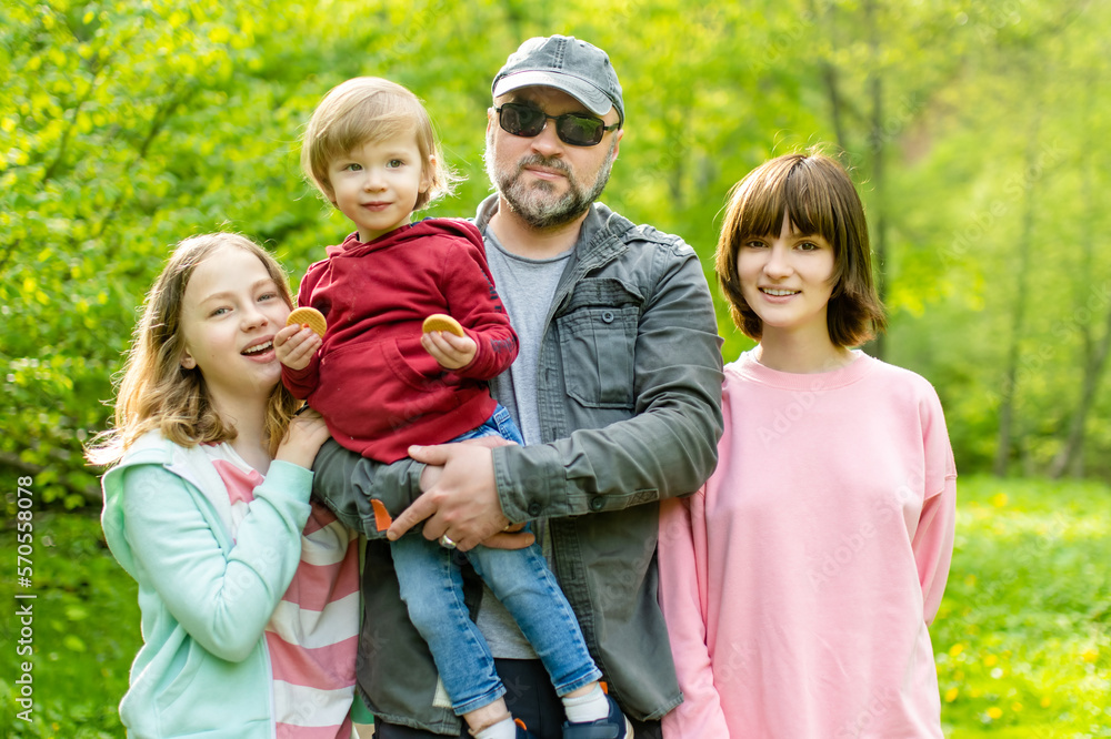 Young father and his three kids hiking in the woods. Family of four having fun on a walking trail on sunny spring day. Young father and his three kids hiking in the woods. Family of four having fun on a walking trail on sunny spring day.