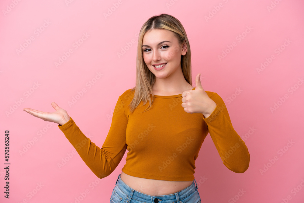Young caucasian woman isolated on pink background holding copyspace imaginary on the palm to insert an ad and with thumbs up Young caucasian woman isolated on pink background holding copyspace imaginary on the palm to insert an ad and with thumbs up