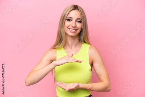 Pretty blonde woman isolated on pink background holding copyspace imaginary on the palm to insert an ad
