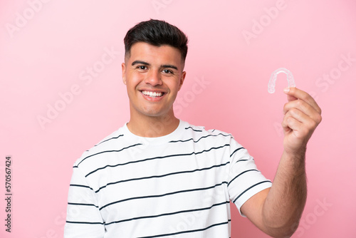 Young caucasian man holding invisaling isolated on pink background with happy expression photo