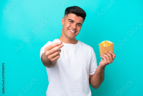 Young caucasian man catching french fries isolated on blue background making money gesture © luismolinero