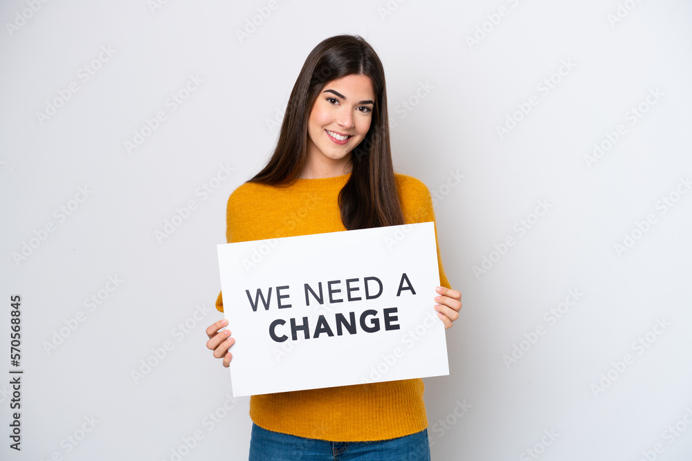 Young Brazilian woman isolated on white background holding a placard with text We Need a Change with happy expression Young Brazilian woman isolated on white background holding a placard with text We Need a Change with happy expression