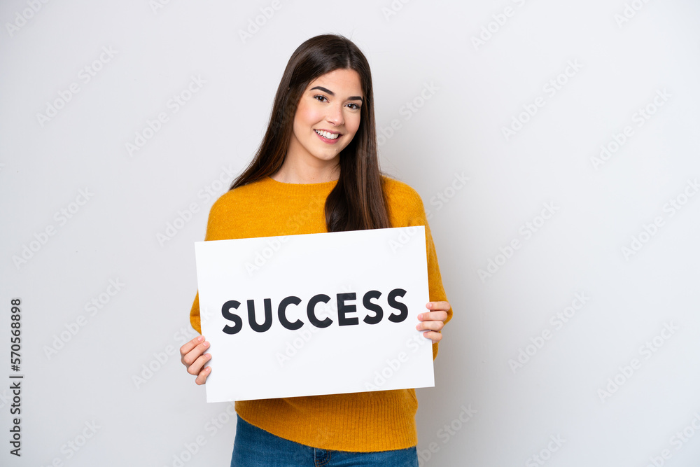 Young Brazilian woman isolated on white background holding a placard with text SUCCESS with happy expression Young Brazilian woman isolated on white background holding a placard with text SUCCESS with happy expression