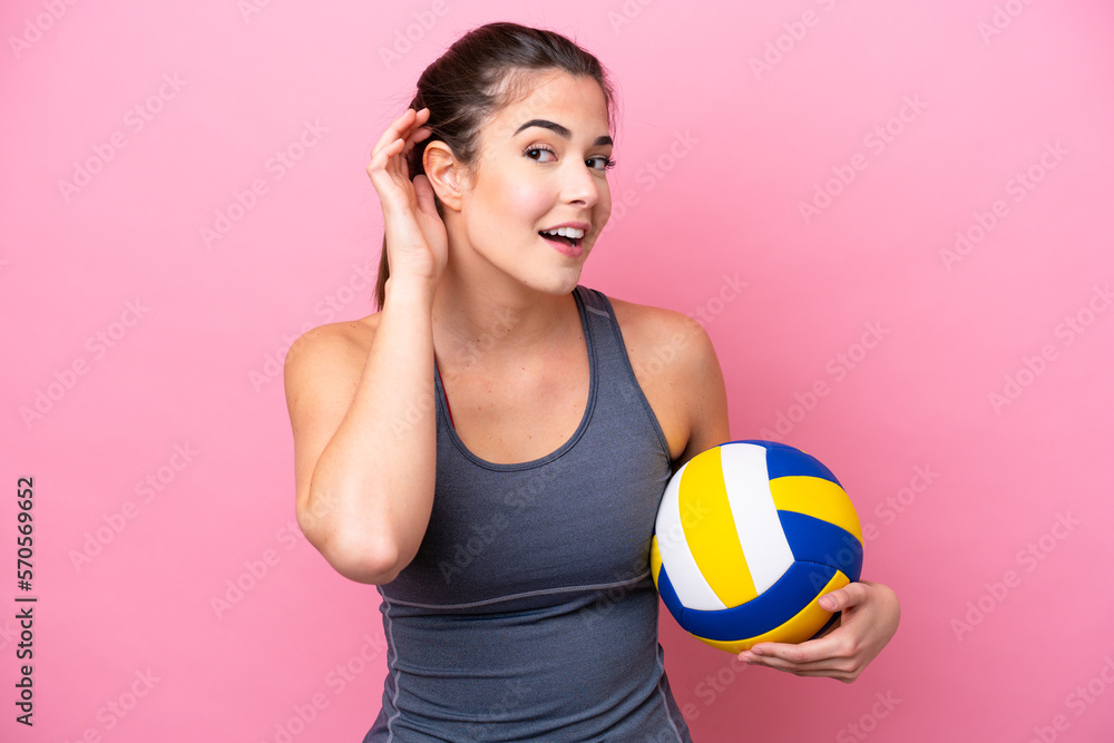 Young Brazilian woman playing volleyball isolated on pink background listening to something by putting hand on the ear