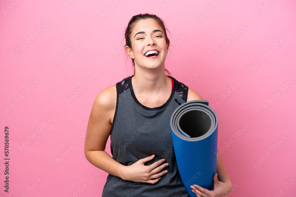 Young Brazilian sport woman going to yoga classes while holding a mat isolated on pink background smiling a lot Young Brazilian sport woman going to yoga classes while holding a mat isolated on pink background smiling a lot