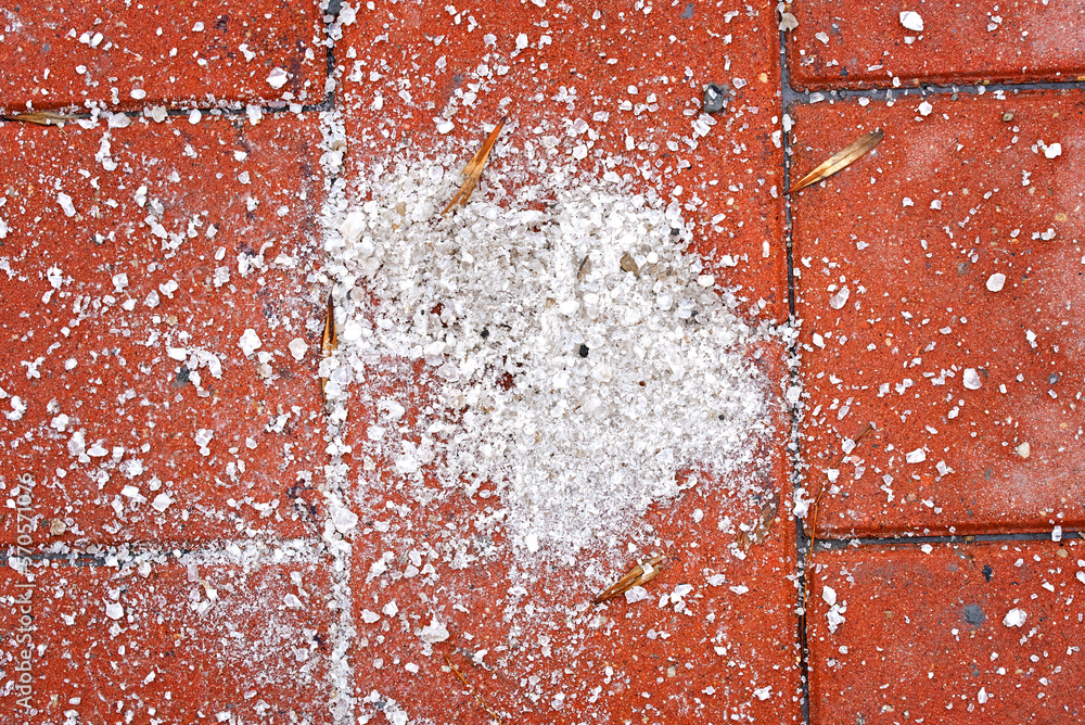 Salt grains on paving slabs closeup. Sprinkle salt on icy sidewalk
