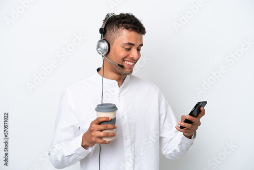 Telemarketer Brazilian man working with a headset isolated on white background holding coffee to take away and a mobile