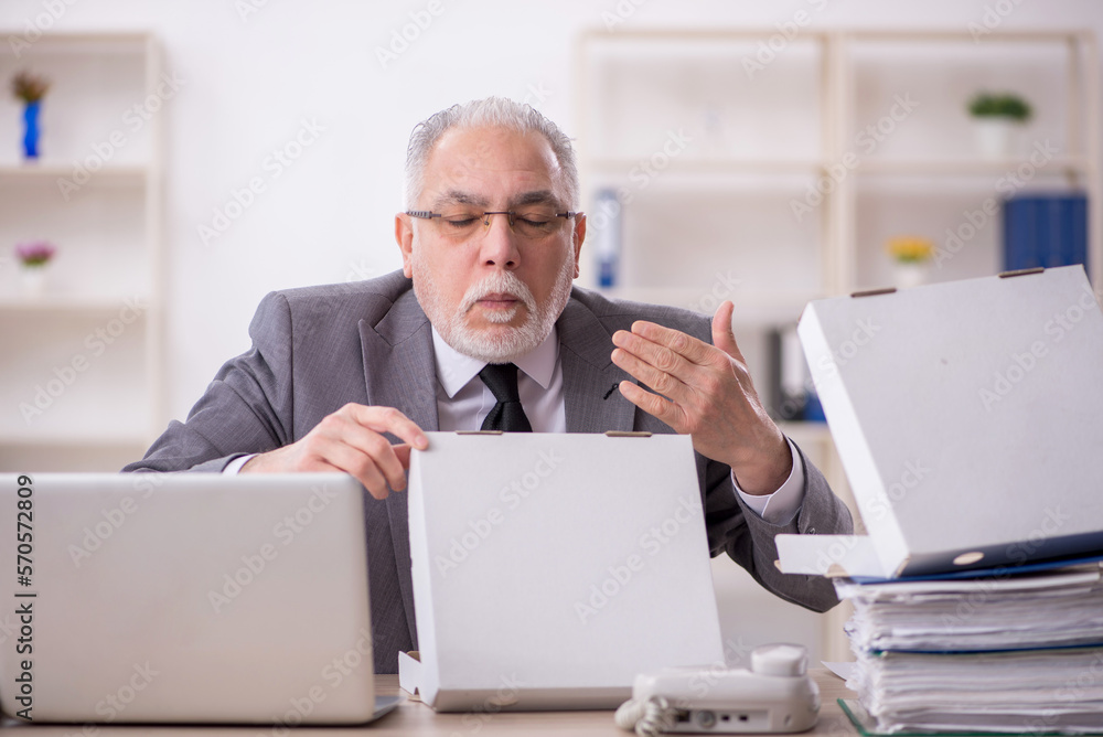 Old male employee eating pizza in the office Old male employee eating pizza in the office