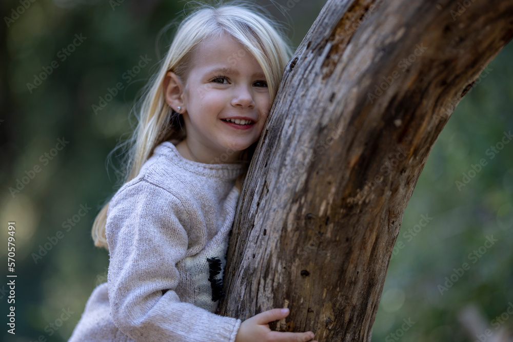 Smiling blonde little girl leaning on fallen tree Smiling blonde little girl leaning on fallen tree