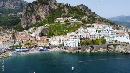 Aerial drone footage of the Marina Grande beach, town hall, Sant'Andrea duomo bell tower in Amalfi coast, Campania, Italy. Parasol, sun loungers, people swimming and colourful cliff villas from above photo