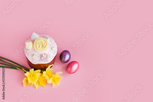 Traditional russian Easter ortodox cake with daffodil flower and colorful eggs on light pink background. Kulic, Kulich, Paska homemade bread with glaze. Spring christian holiday. Festive celebration photo