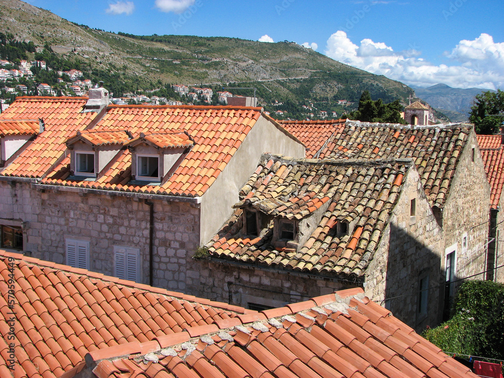 A charming view of several terra cotta coloured rooftops in Dubrovnik, Croatia on a sunny day with a blue sky with clouds as a backdrop.  Image has copy space.