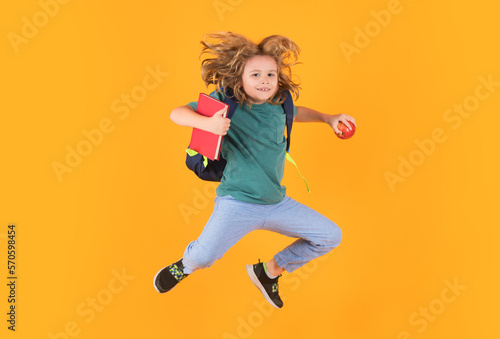 Kid jump and enjoy school. Funny child school boy jumping on a yellow studio background.