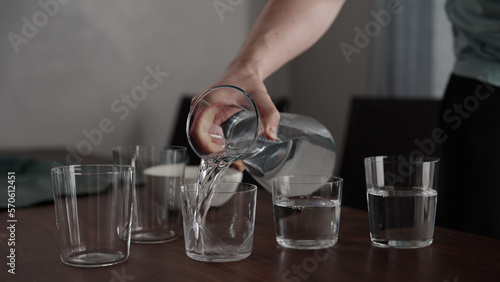 Man pour water into glasses from carafe on walnut table photo
