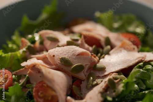 Salad with roasted turkey and cherry tomatoes decorated with pumpkin seeds in blue bowl