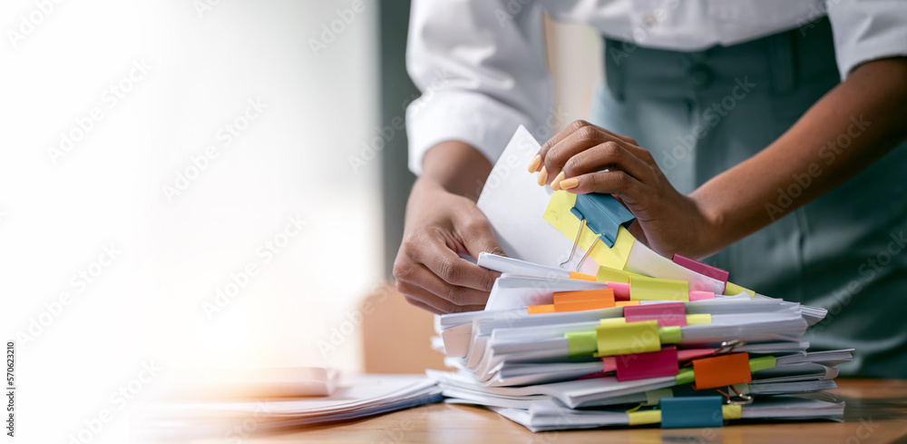 Black skin woman hands working in Stacks of paper files for searching and checking unfinished document achieves on folders papers - obrazy, fototapety, plakaty 