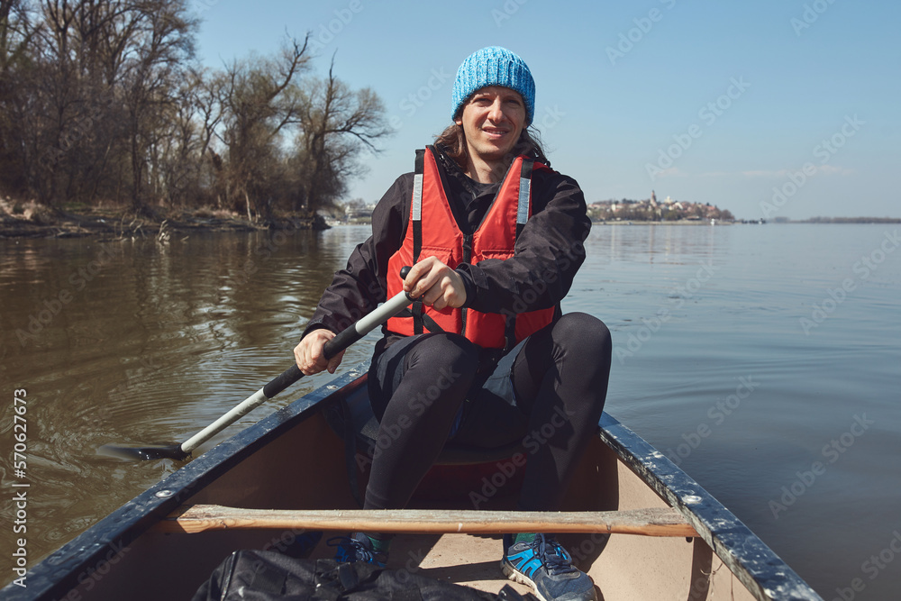 Man paddling in a canoe on a Danube river in urban area, small recreational escape, hobbies and sports outdoors.