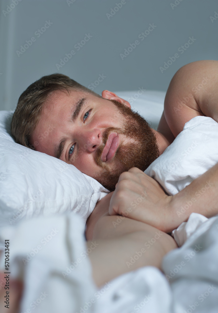 Young sad depressed unhappy worried man in the bed in bedroom at home in the morning lying under white blanket suffering from insomnia problems with sleep at night Young sad depressed unhappy worried man in the bed in bedroom at home in the morning lying under white blanket suffering from insomnia problems with sleep at night