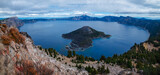 Panoramic view of Crater Lake with Wizard Island in the center and a sky with many clouds.