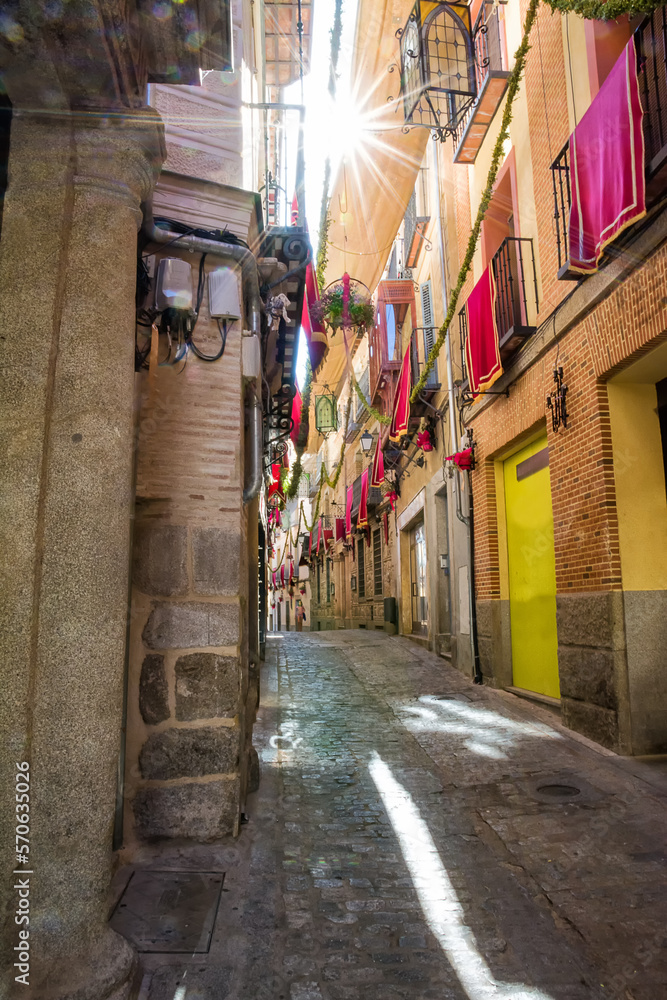 Narrow alleys of Toledo with shade cover, decorated balconies and sunbeams