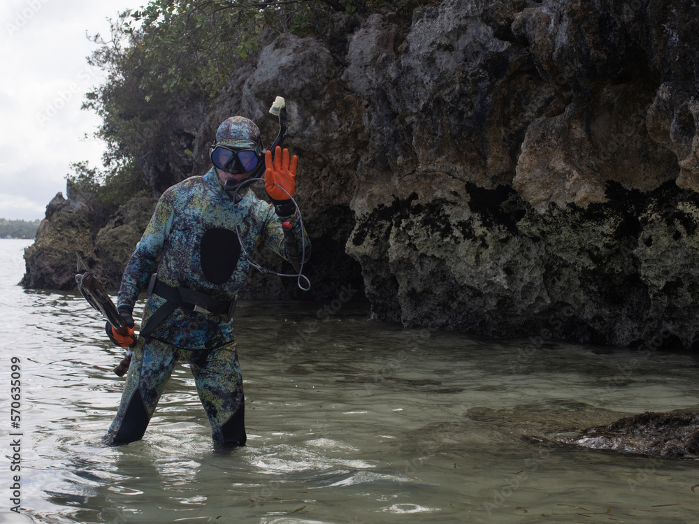 a man in a wetsuit, with camouflage coloring, is preparing for spearfishing, with an underwater rifle in his hands