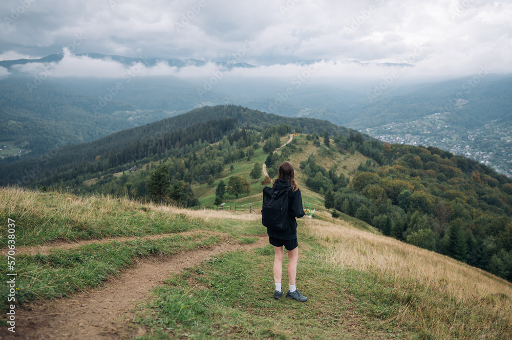 A woman tourist in dark casual clothes walks along a path in the mountains against the background of beautiful landscapes of the Ukrainian Carpathians, turns to look at the views.