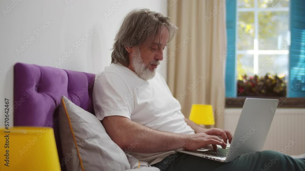 Mature man is working with laptop in bed. Realtime Mature man is working with laptop in bed. Realtime