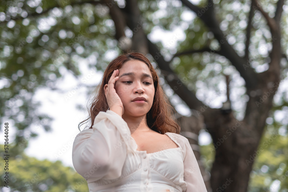 A troubled young lady looks down and touches the temple of her head as she experiences headache. A troubled young lady looks down and touches the temple of her head as she experiences headache.