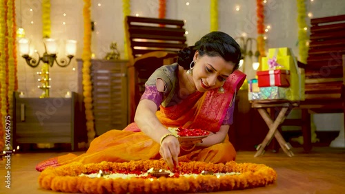 Happy traditional indian girl decorating Rangoli with flowers for diwali festival celebration on floor at home - concept of culture, custom and festive preparation.