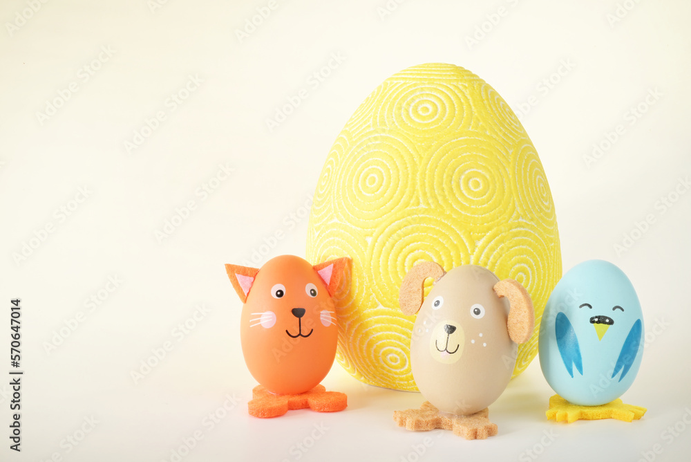 Trzy kolorowe zwierzątka zrobione z jajek stojące obok dużej wielkanocnej pisanki na jasny tle - obrazy, fototapety, plakaty 