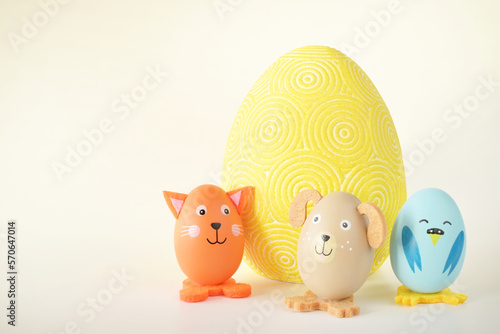 Trzy kolorowe zwierzątka zrobione z jajek stojące obok dużej wielkanocnej pisanki na jasny tle