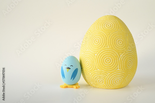 niebieski wielkanocny kurczak zrobiony z jajka stojący obok dużej żółtej pisanki na jasnym tle