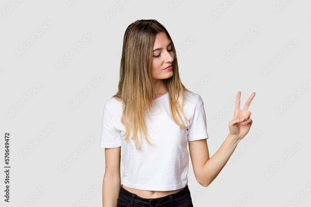 Young blonde posing for a portrait isolated, exuding natural beauty and radiance joyful and carefree showing a peace symbol with fingers. Young blonde posing for a portrait isolated, exuding natural beauty and radiance joyful and carefree showing a peace symbol with fingers.