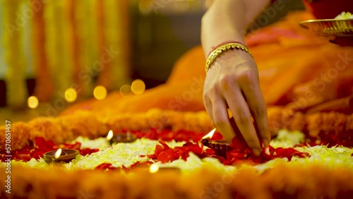 Close up shot of woman hands decorating Rangoli design with flowers for diwali festival celebration on floor at home with diya or lamps - concept of festival preparation, Indian culture and planning.