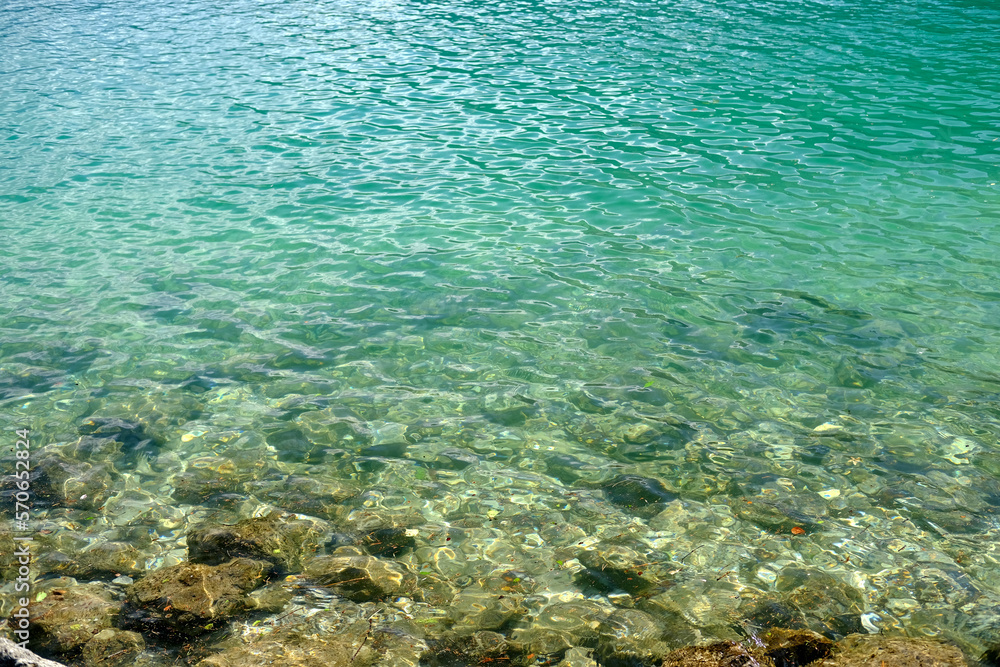 Fototapeta premium blue sea, ocean waves, water with bubbles, rocks near the shore, texture, water natural resources concept, beauty of nature, vacation by the reservoir, water sports, background, texture for designer