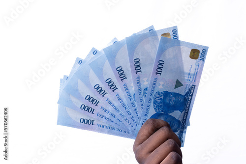 A black hand holding a spread of the New Nigerian currency / money, the 1000 Naira note on a white background